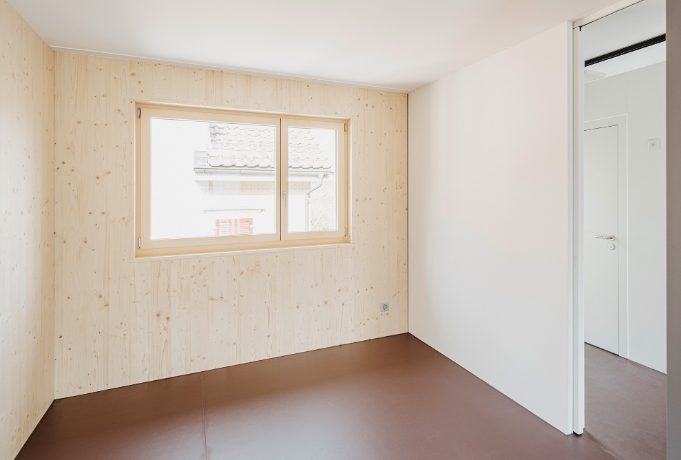 helles Zimmer mit Fenster und Holzwänden in der Mikrowohnung
