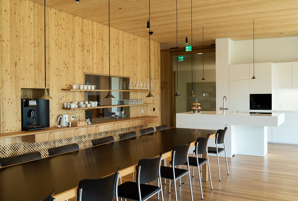 Interior view of the kitchen with abundant timber, a long black table and a cooking island, plus white cabinets