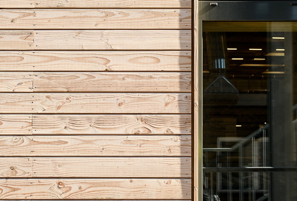 Detailansicht der Uvood-behandelten horizontal verlegten Holzfassade. Daneben der Ausschnitt einer Fensterscheibe. 