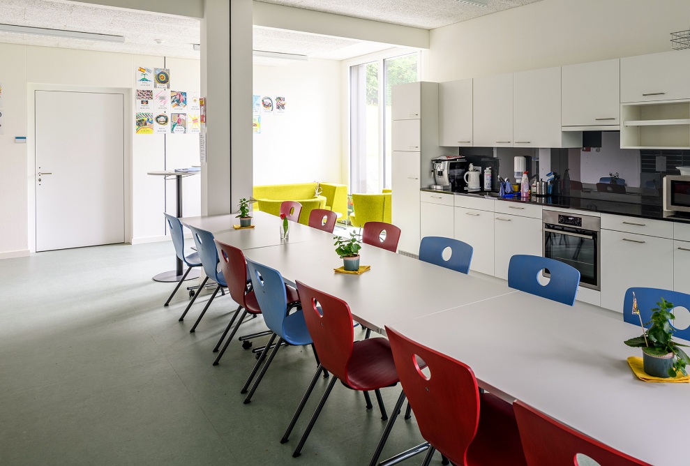 Innenansicht der Küche im Schulhaus Grenzhof Luzern mit langem Tisch, Küchenzeile und Sitzecke