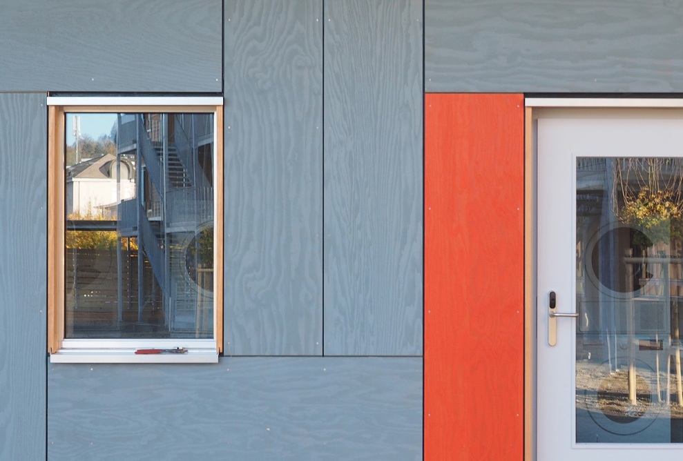 Photograph of the grey and red facade of the Grosshof asylum centre with enlarged shot of windows and doors