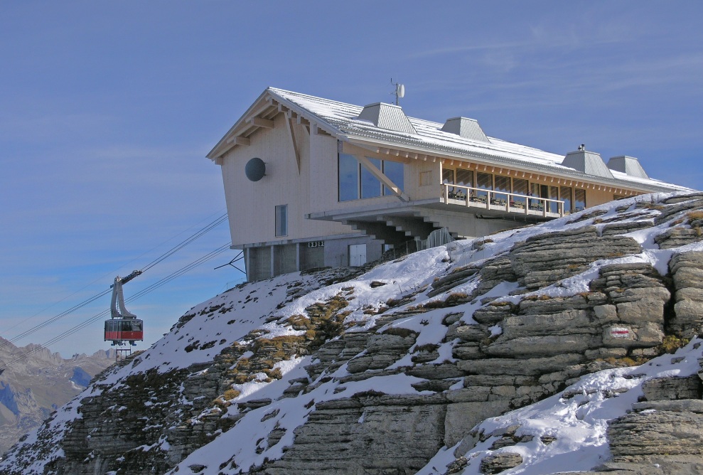 Vue extérieure de l’auberge de montagne de Chäserrugg avec téléphérique et roches au premier plan.