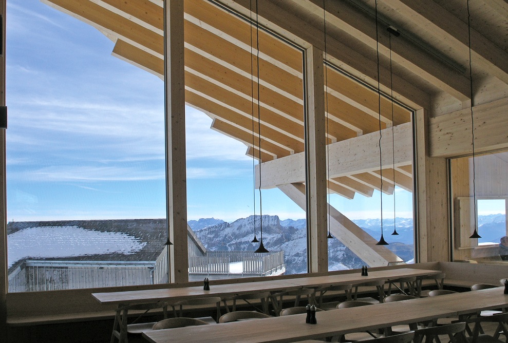 Chäserrugg summit restaurant dining area with tables and chairs and panoramic mountain views with blue sky