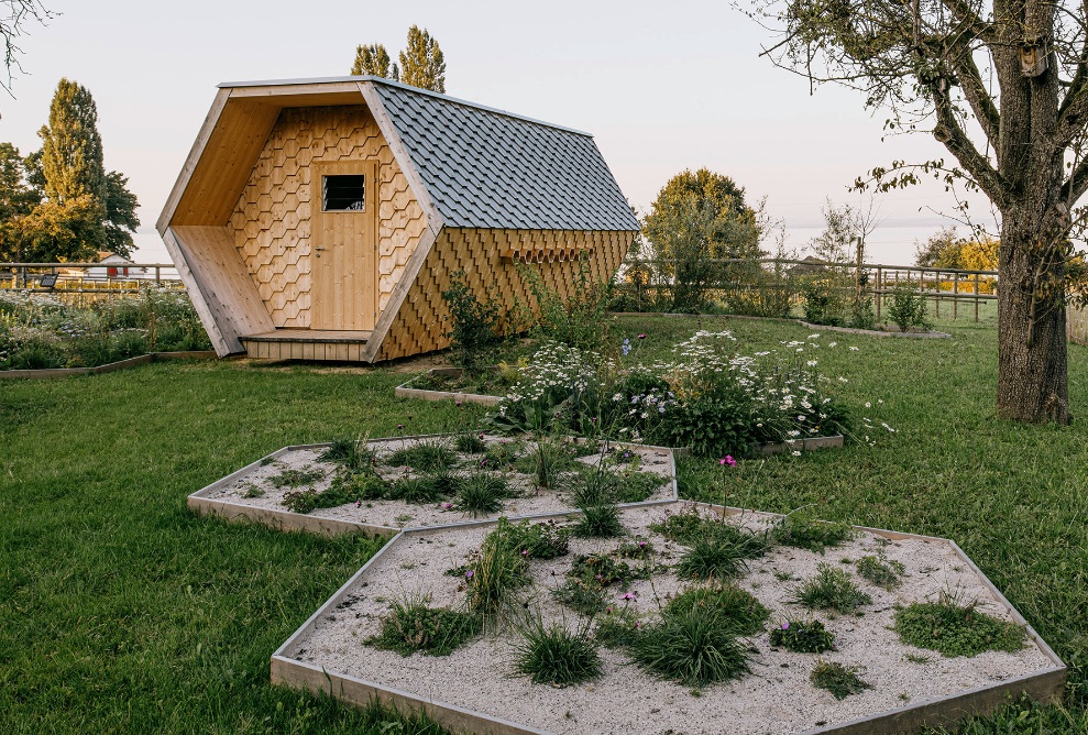 Full view of the bee house in the garden with trees and shrubs