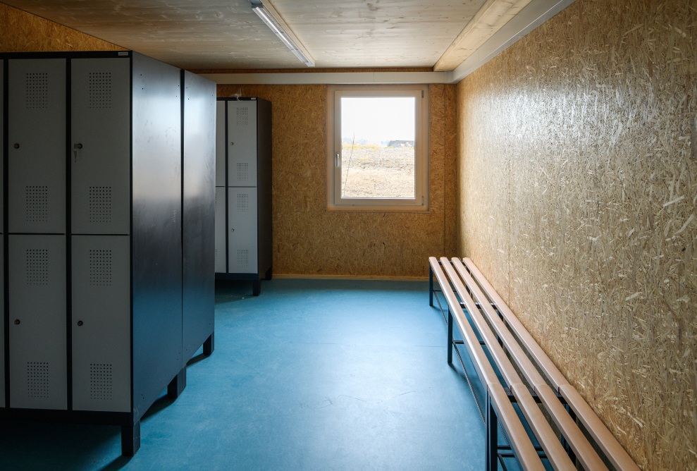 Blick in die Garderobe für die Mitarbeitenden der Bio-Bäckerei Lehmann. Innenausbau mit Garderobenschränken und Bänkchen zum Umkleiden. Blauer Fussboden.