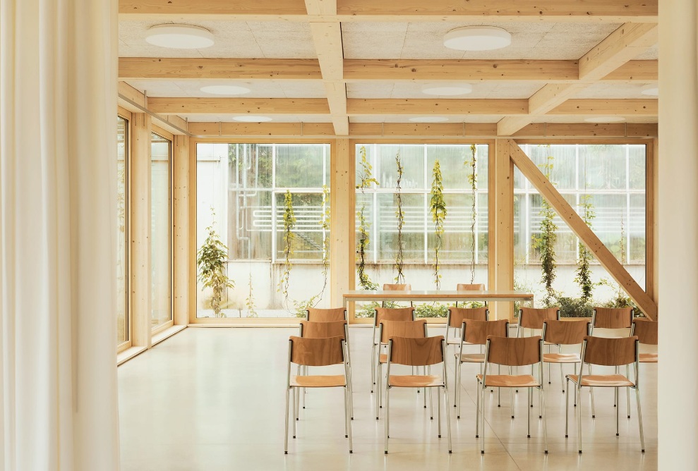 Blick in den hellen Vortragsraum mit Holzstühlen und Glaswand im Hintergrund im botanischen Garten in St. Gallen. 