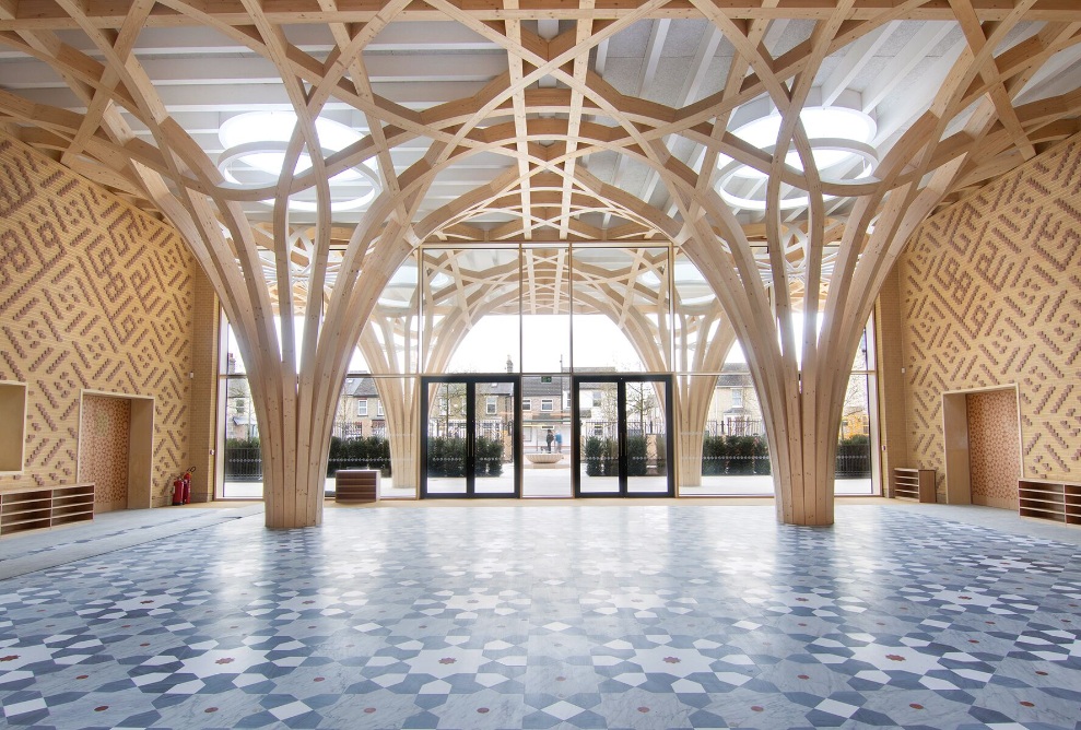 Die baumartige holzige Tragstruktur dominiert den Eingangsbereich der Cambridge Mosque. Der Fussboden ist mit einem grau-blauen Plattenmosaik gestaltet und die Wände mit zweifarbigen Klinkersteinen mit orientalischen Motiven. 