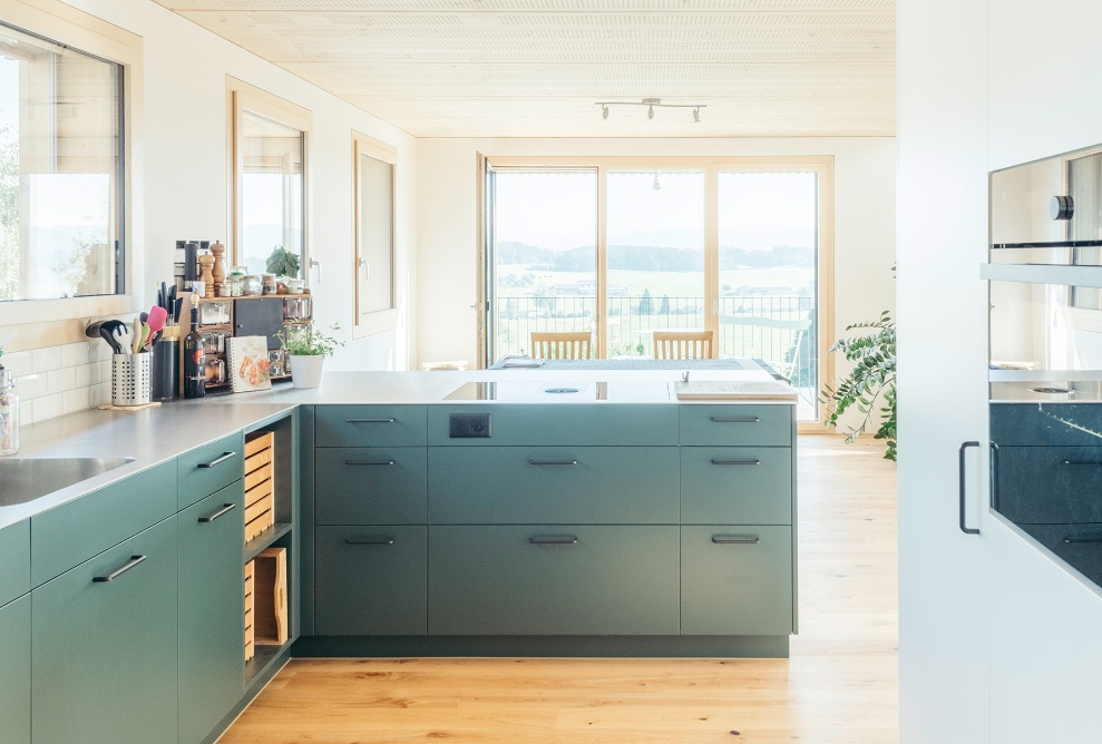 Die moderne Küche mit graugrüner Front ist zum Essbereich mit Balkon hin offen.