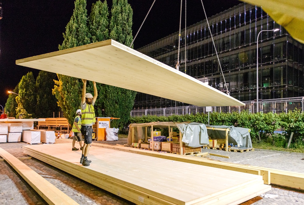 The photograph shows two construction workers with wooden panels after sunset