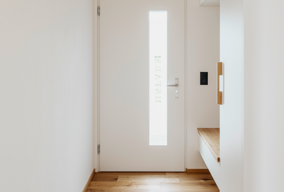 Entrée de la maison avec porte et murs blancs, plafonds et sol en bois.