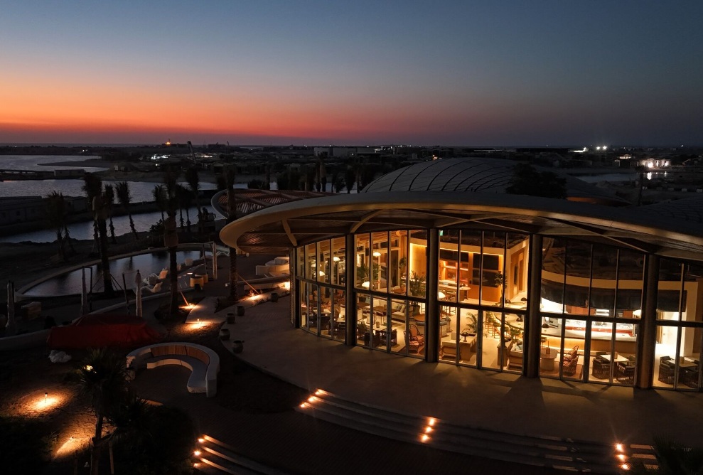 Vue aérienne du club-house de golf illuminé sur l’île de Shura au coucher du soleil avec toit courbé et façade vitrée