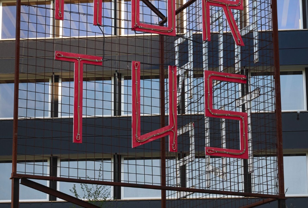 Roter HORTUS-Schriftzug auf Metallgitter vor der dunklen Gebäudefassade mit Fenstern