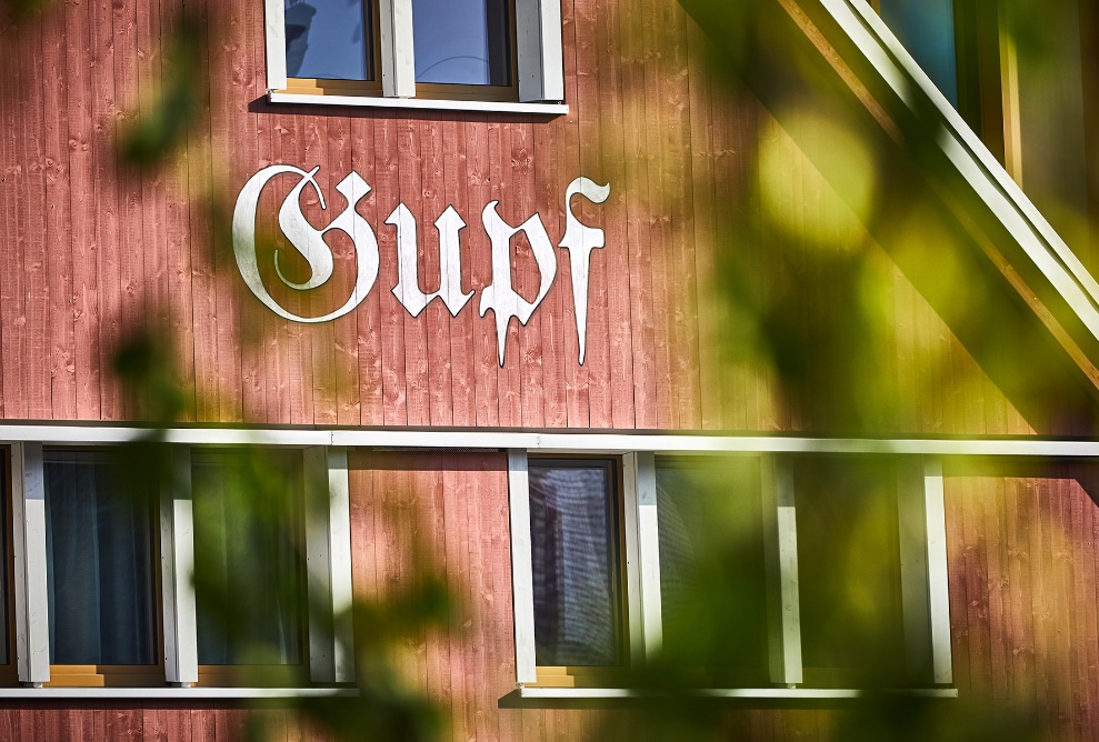 La façade du Dorfhus Gupf est en bois d'épicéa laqué rouge avec des cadres de fenêtres blancs.