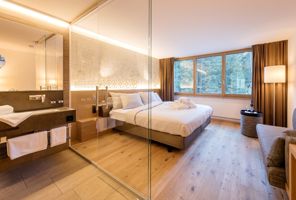 A glazed door separates the spacious bedroom from the bathroom. The room is furnished to a high standard and is bathed in light thanks to the large window.