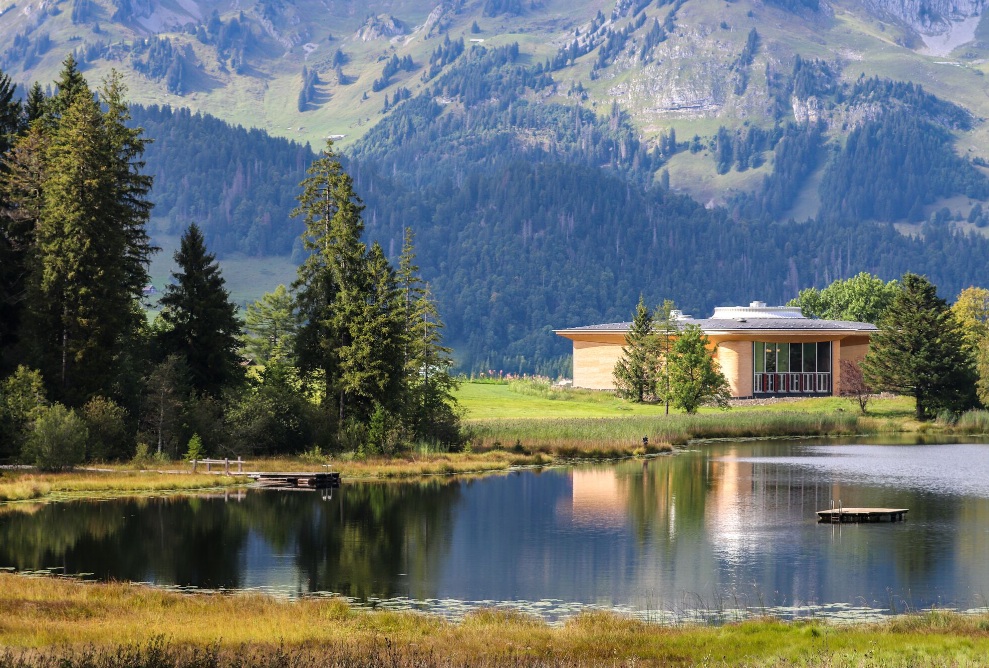 Panoramaaufnahme des Klanghauses Toggenburg am Ufer des Schwendisees, eingebettet in eine eindrucksvolle Berglandschaft.