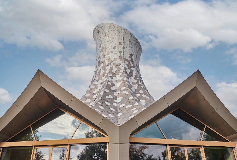 The cantilever timber roof, designed as a prismatic shell structure, is surrounded by irregularly shaped sheet metal sheds. 