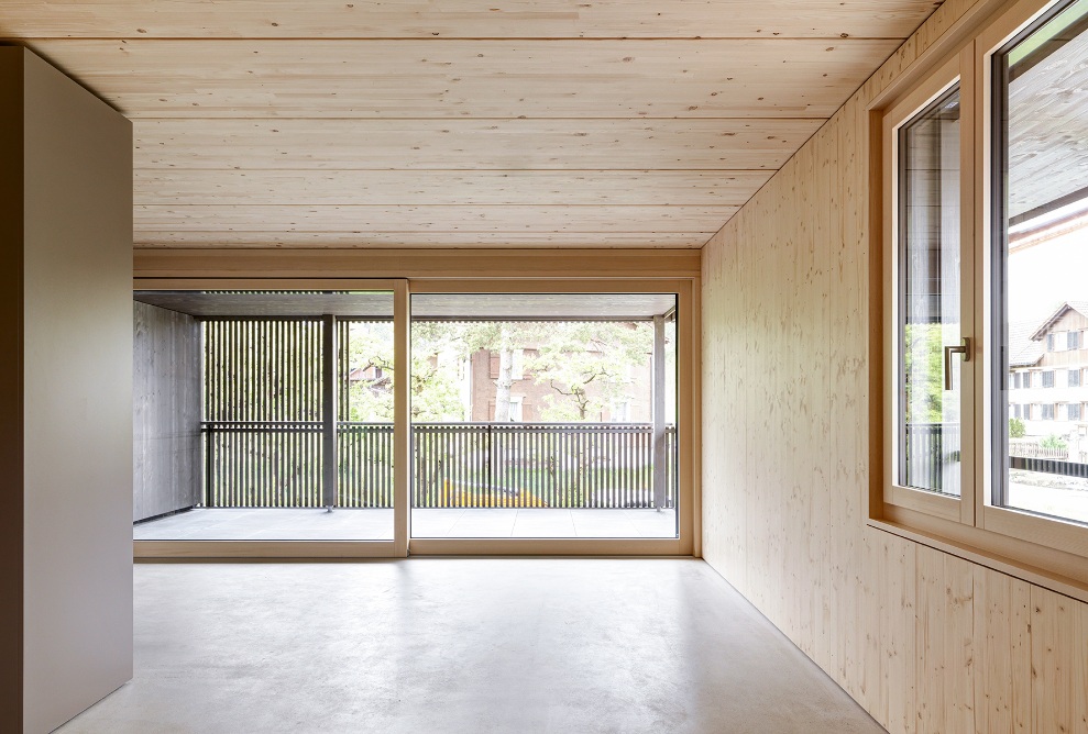 Séjour lumineux avec murs, plafonds et sols en bois, grandes fenêtres et balcon