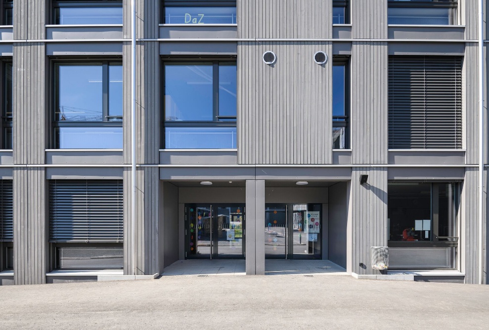 Main entrance of the modern Herti school building with large windows and wooden facade