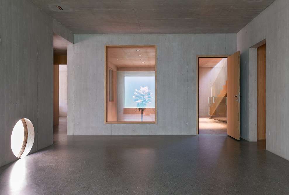 Pièce dotée de murs en béton, de portes en bois et de grandes fenêtres placées de façon inhabituelle dans le socle de la Sutra House.