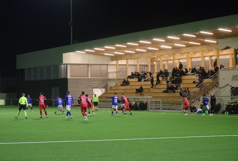 Fussballspiel vor der beleuchteten Holztribüne im Stadion Gossau