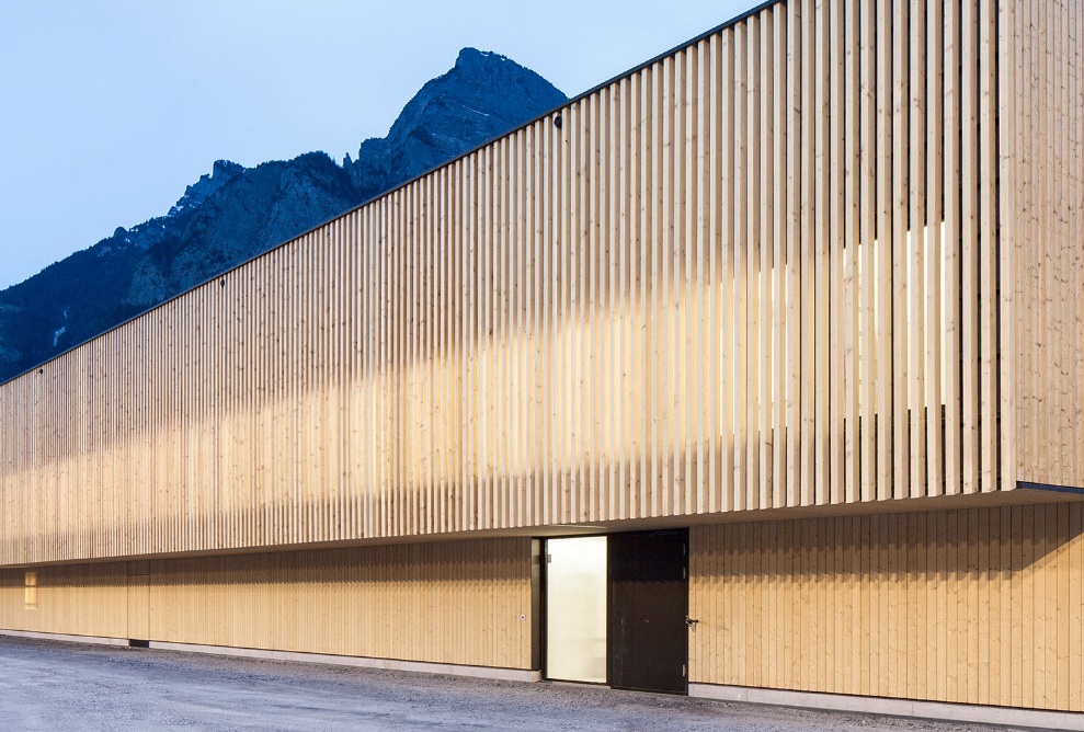 Der moderne Holzbau des RSA Sargans steht in Abenddämmerung vor einem Bergmassiv.