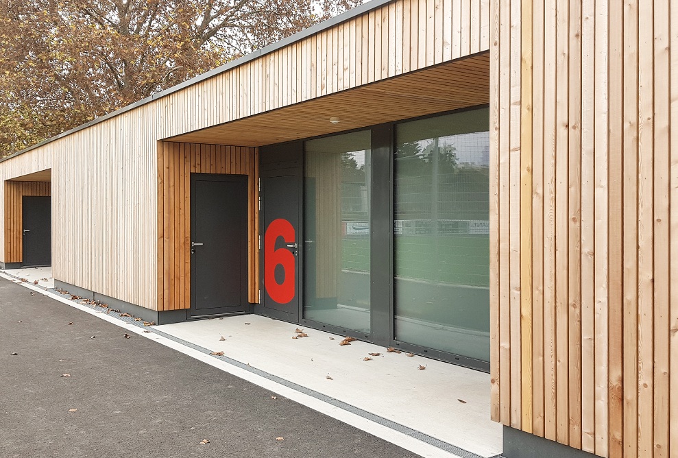 Entrée du vestiaire du bâtiment d’extension avec façade en bois, au lettrage bien voyant