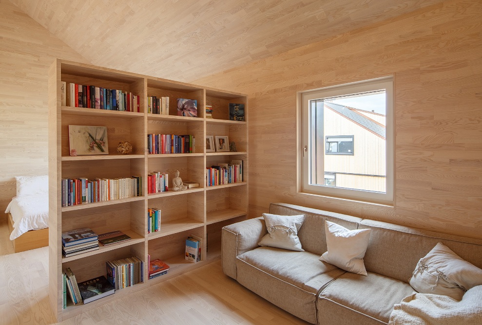 Blick in den Wohnraum mit einem vollständig in Holz ausgekleideten Innenausbau mit Sofa und Büchergestell einer Wohnung. 