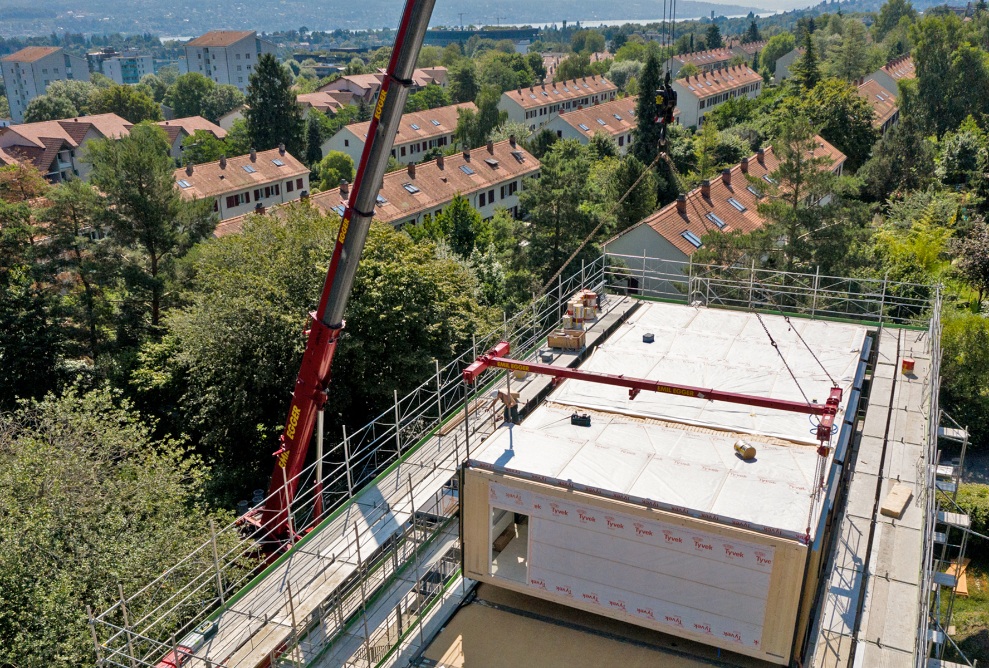 Blick aus der Luft auf das Dach des Schulhauses Friesenberg mit fünf bereits platzierten Holzmodulen auf dem Dach.