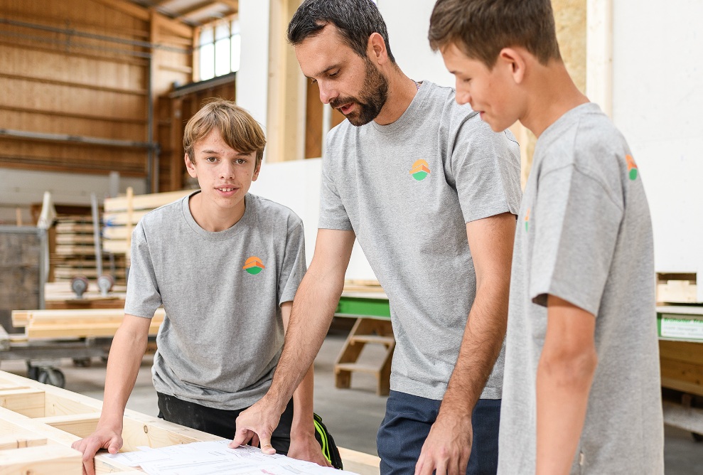 A group of 2 apprentices and an instructor, mid-discussion. One person is looking at the camera, 2 are looking at a diagram.