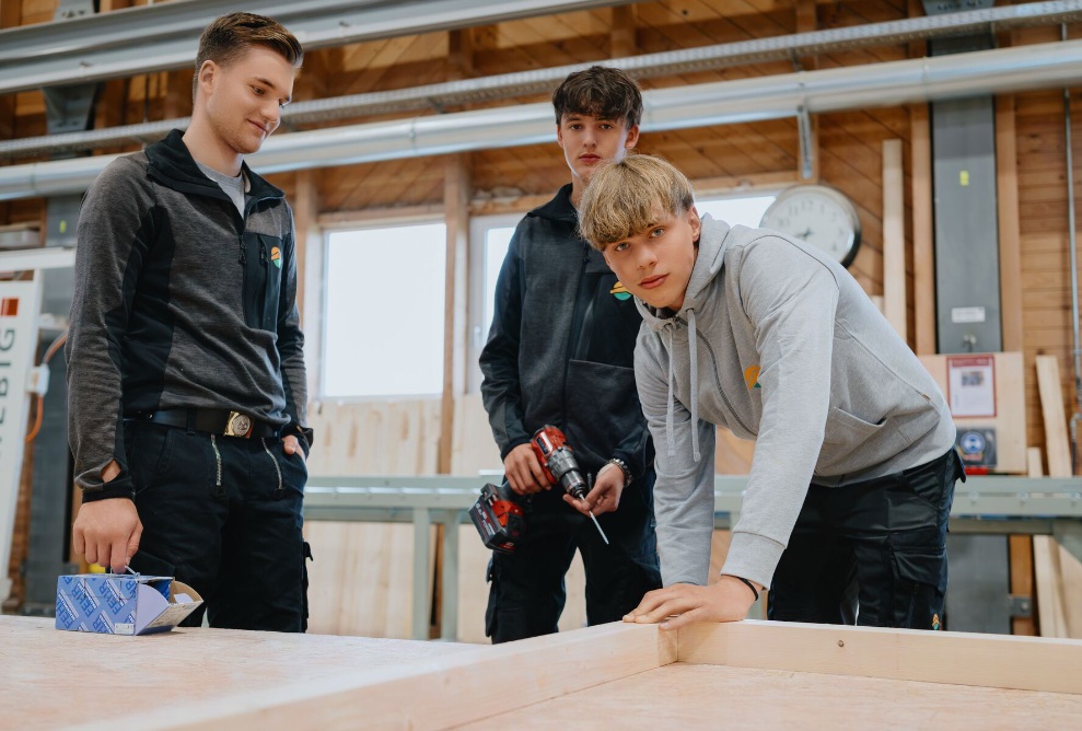 A group with 3 learners. One person is looking at the camera, 2 people are looking at the workpiece.