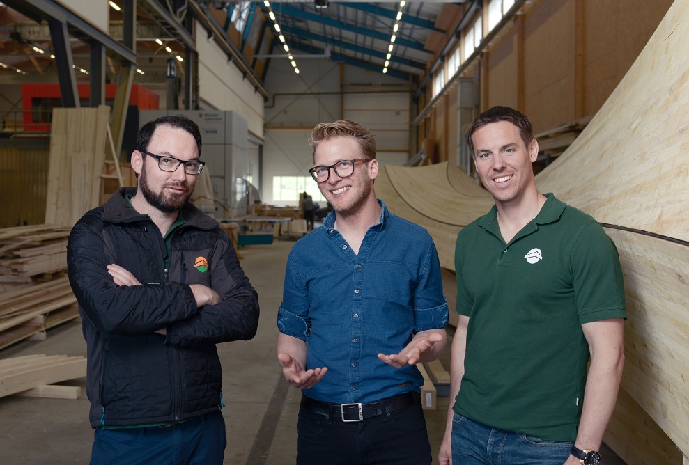 Gruppe von Quereinsteigern in der Produktionshalle mit einem Holzobjekt im Hintergrund