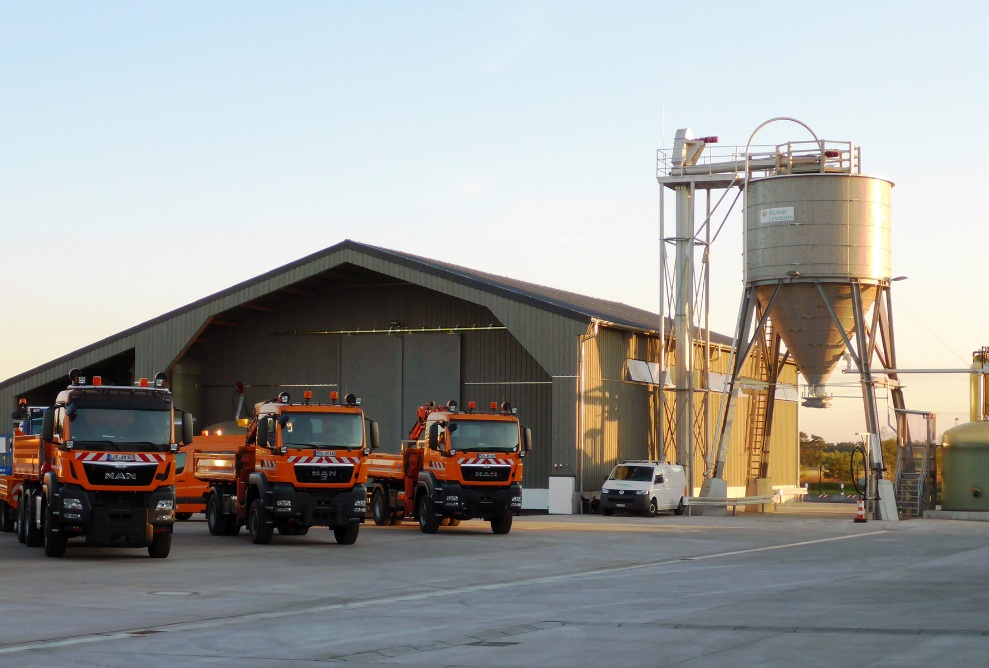 Installation complète à Fahrbinde (Allemagne), composée d’un entrepôt, d’un silo en bois et d’une centrale à saumure, devant lesquels sont stationnés trois camions du service hivernal