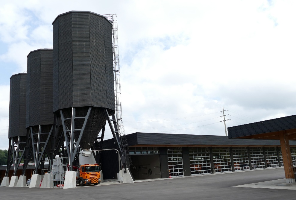 Drei schwarze zwölfeckige 900 m³ Silos aus Holz neben modernem Werkhofgebäude mit gleicher schwarzer Fassade platziert