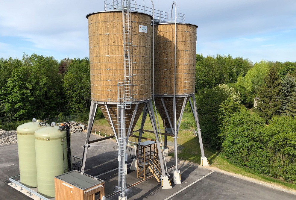 Zwei runde 250 m³ Silos aus Holz auf Stahlunterbau mit Soletechnik auf einem Werkhof platziert